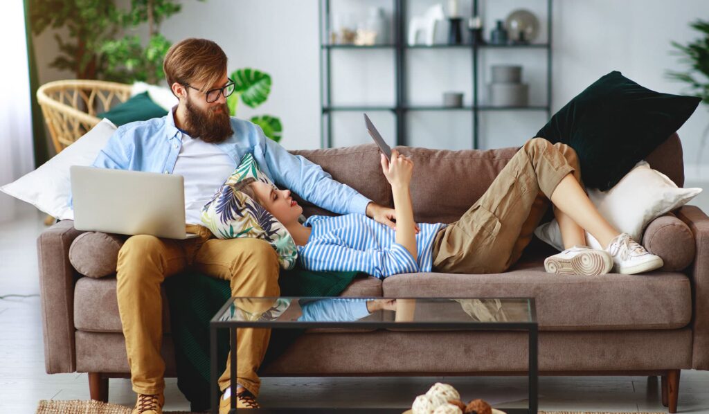 Comfortabele thuiswerkplek met jonge vrouw en man op bank, werken en ontspannen in gezellige woonkamer, flexibele thuiswerkoplossingen, moderne interieur, Van de Ven & Meijer Advies B.V.